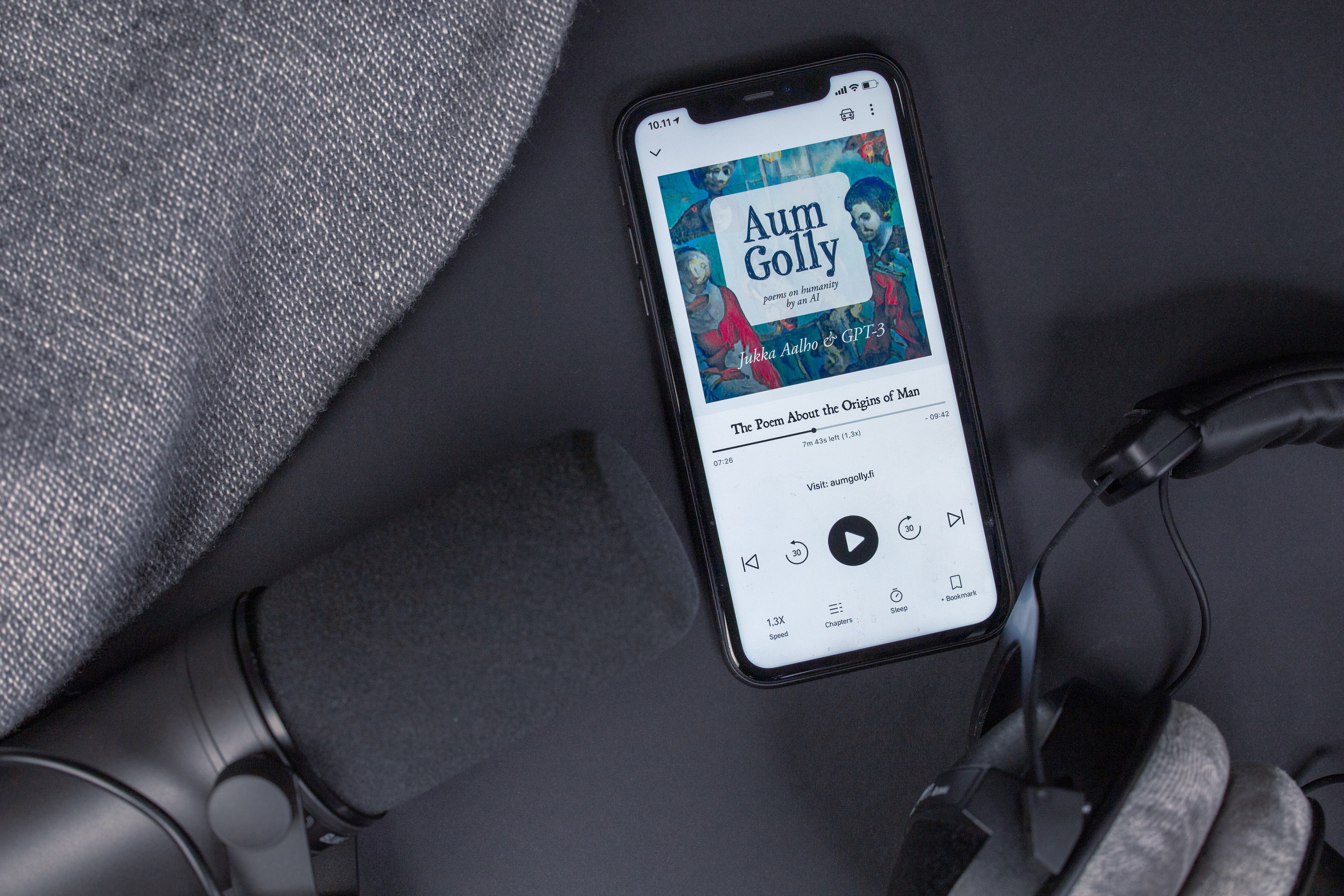 Flatlay audiobook with headphones, black phone and microphone on black background and different shades of gray.