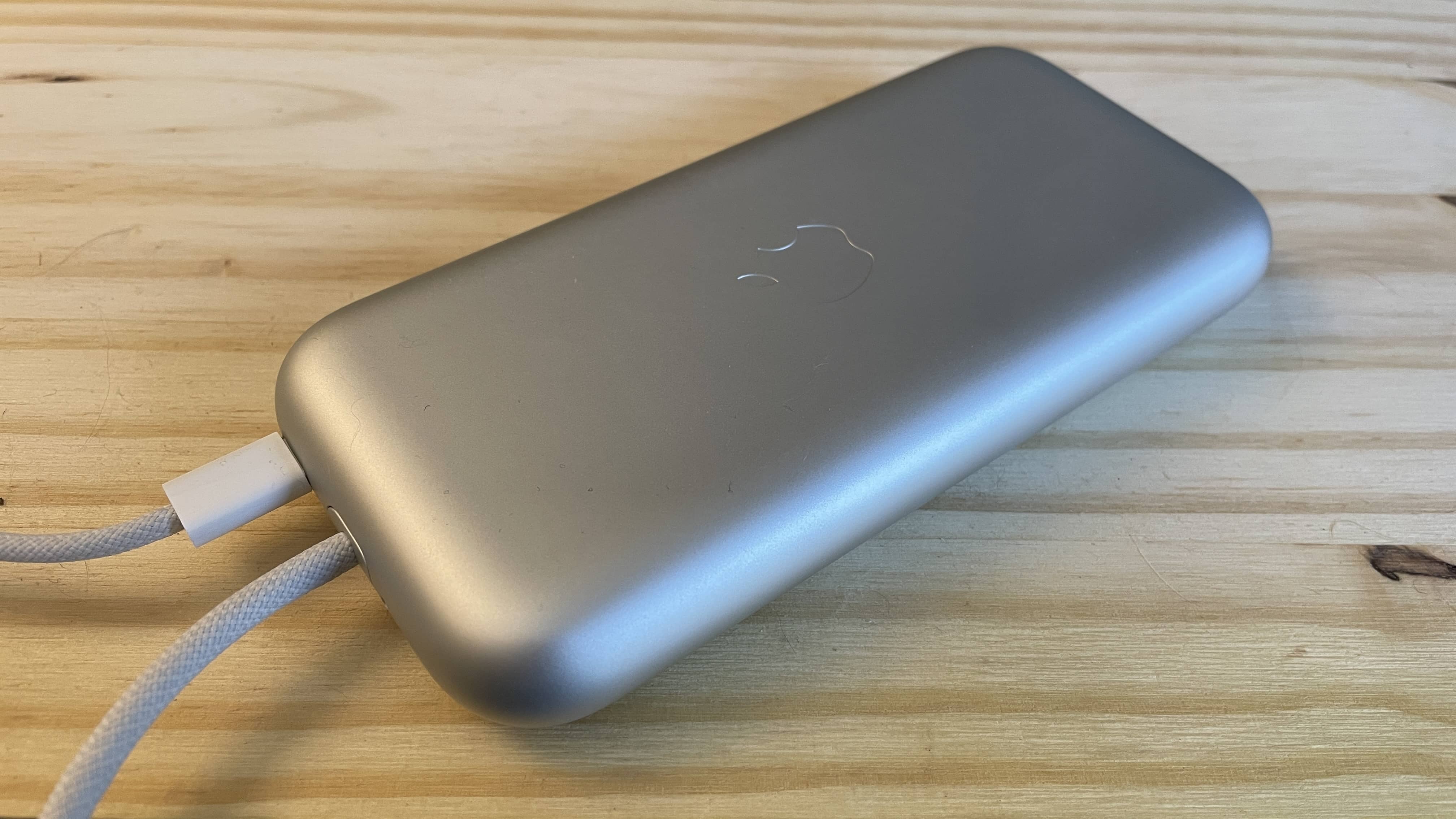 Vision Pro battery plugged in, sitting on a pine desk