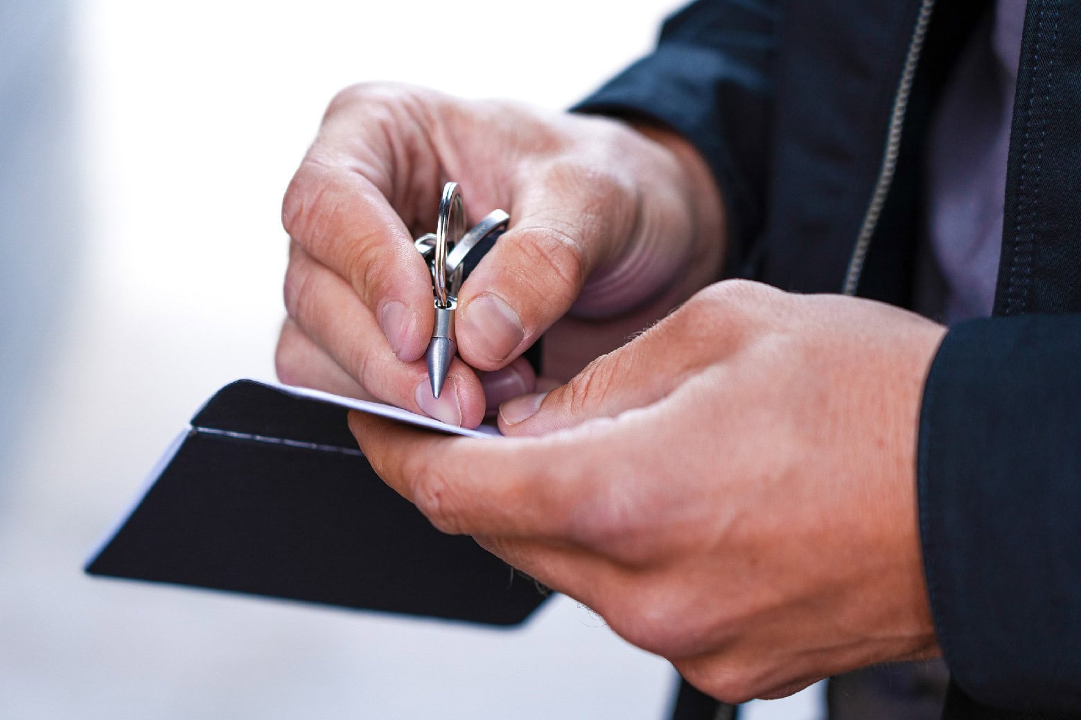person writing on a small notebook using ForeverPen, a small inkless pen that fits on a keychain