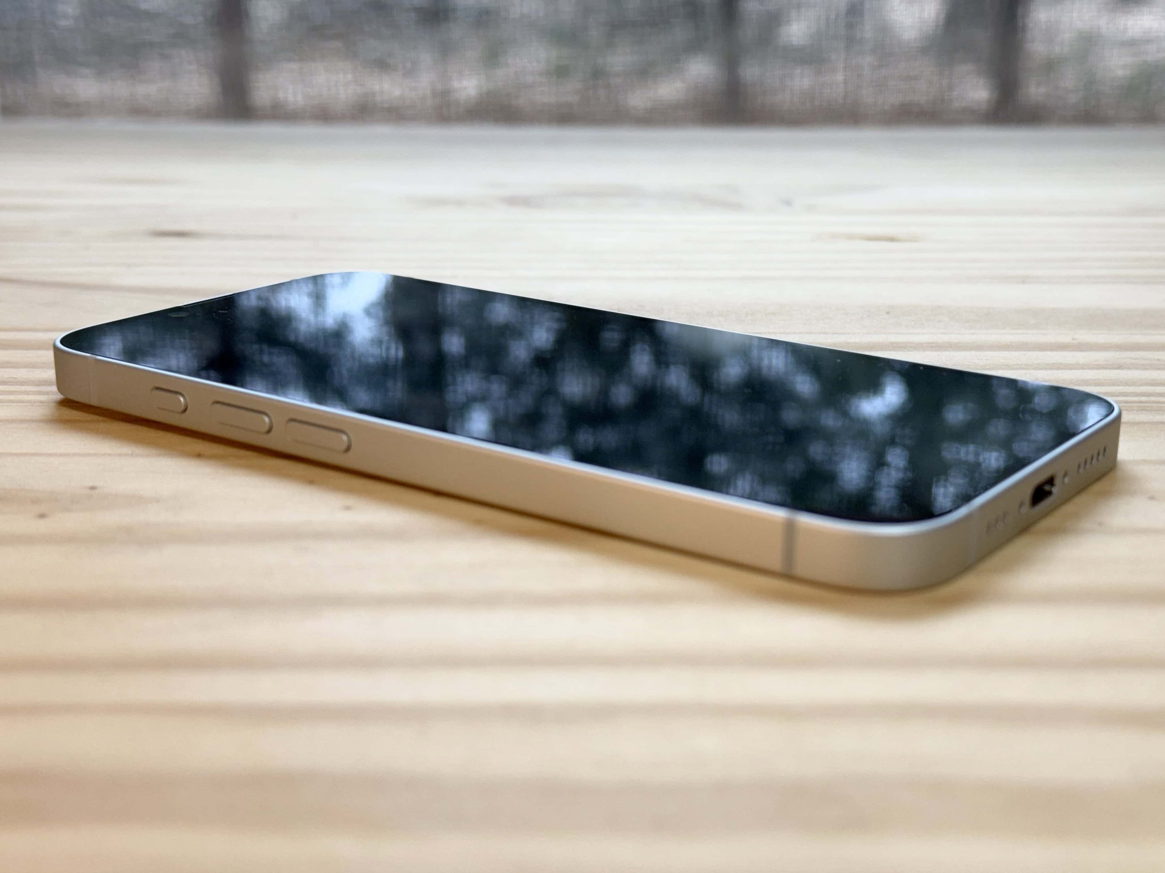 iPhone 16e laying down flat on a pine table surface.