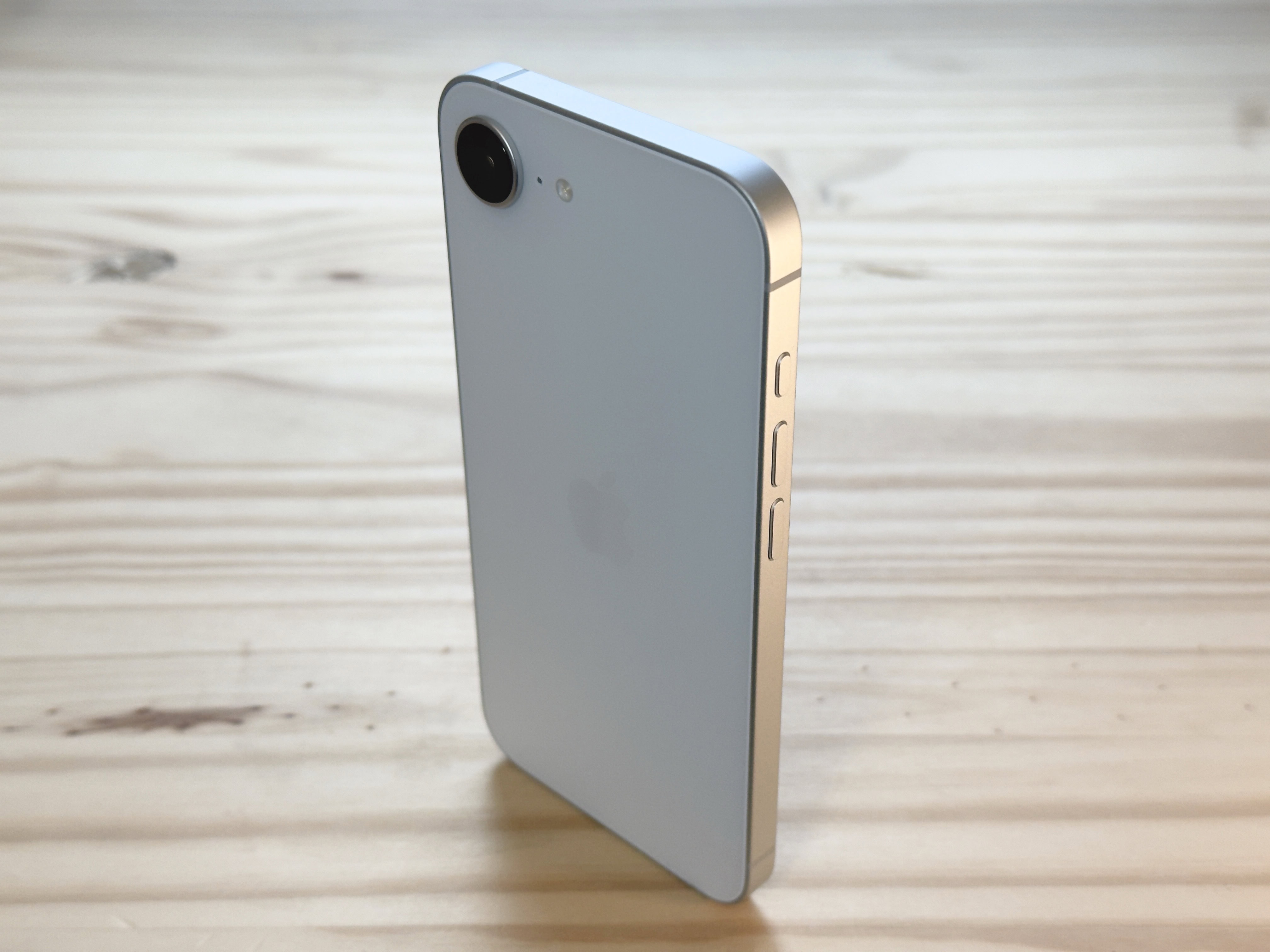 iPhone 16e standing up vertically on a pine table surface, used to illustrate an iPhone 16e review