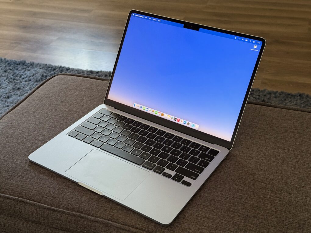 Blue MacBook Air sitting on a gray linen ottoman on a blue fuzzy rug on a gray laminate floor