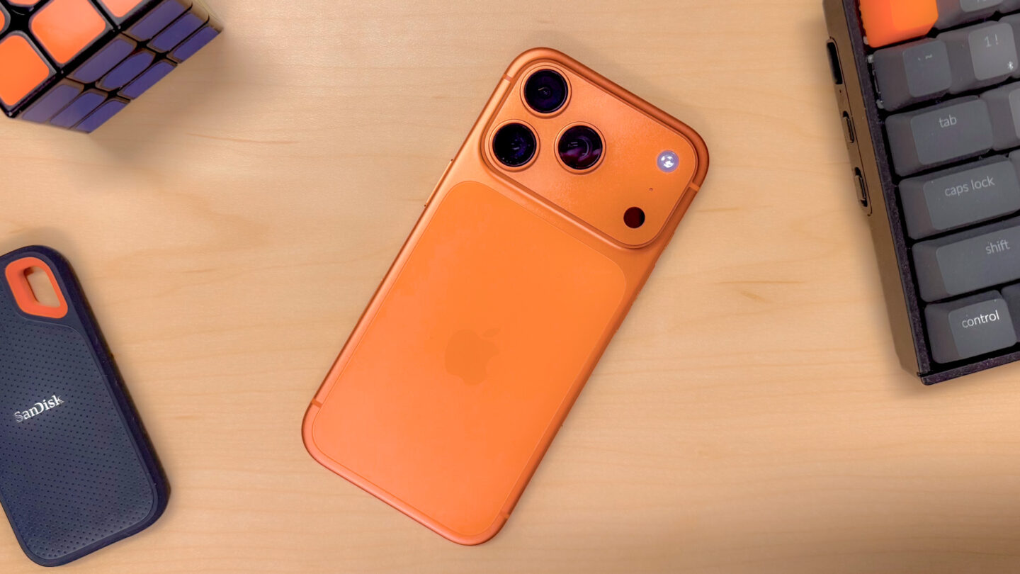 An iPhone 17 Pro in Cosmic Orange, on a desk surrounded by objects with orange accents